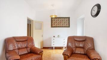 Una habitación con dos sillones de cuero, un tocador blanco, un tapiz decorativo y un reloj de pared.
