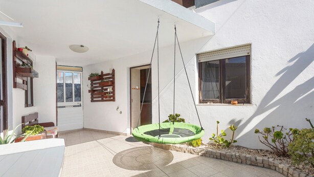 A patio with a hanging swing, a door leading to a room, and a small garden area with plants. - Holiday Home 'D´Aldeia' with Shared Terrace, Private Garden and Wi-Fi (Cela Velha)