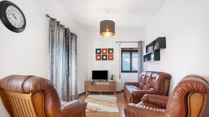 A living room with leather chairs, a TV stand, and a hanging light fixture. - Holiday Home 'D´Aldeia' with Shared Terrace, Private Garden and Wi-Fi (Cela Velha)