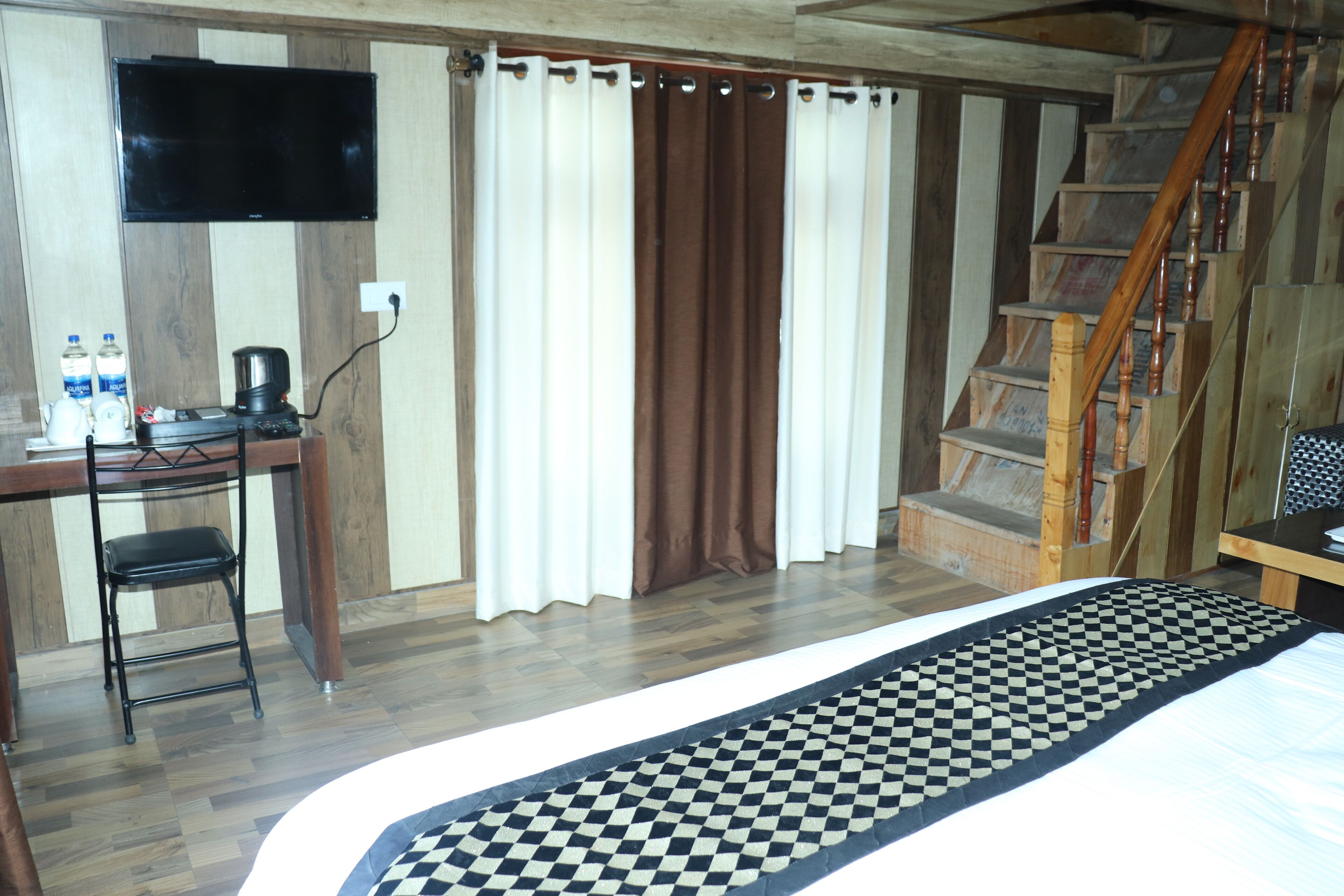 Een slaapkamer met een bed, een bureau met stoel, een televisie en een trap.