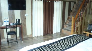 A bedroom with a bed, a desk with a chair, a television, and a staircase.
