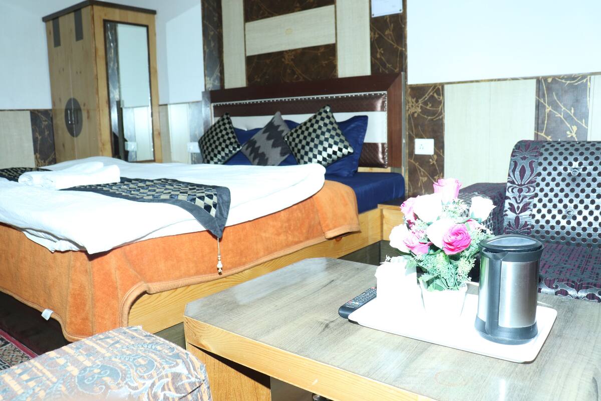 A hotel room with a bed, a wooden nightstand, a table with a vase of flowers, and a chair.