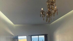 Sala de estar con un sofá, una mesita, una araña y vista al mar a través de una ventana.