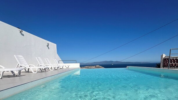 Piscina azul cristalina con sillas de reposo blancas y vista al mar.