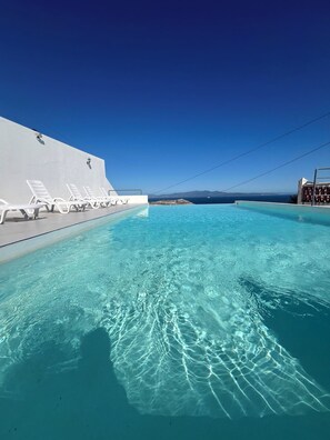A clear blue pool with white lounge chairs and a view of the sea. - Centre Socio-culturel Dr Masmoudi (Belyounech)