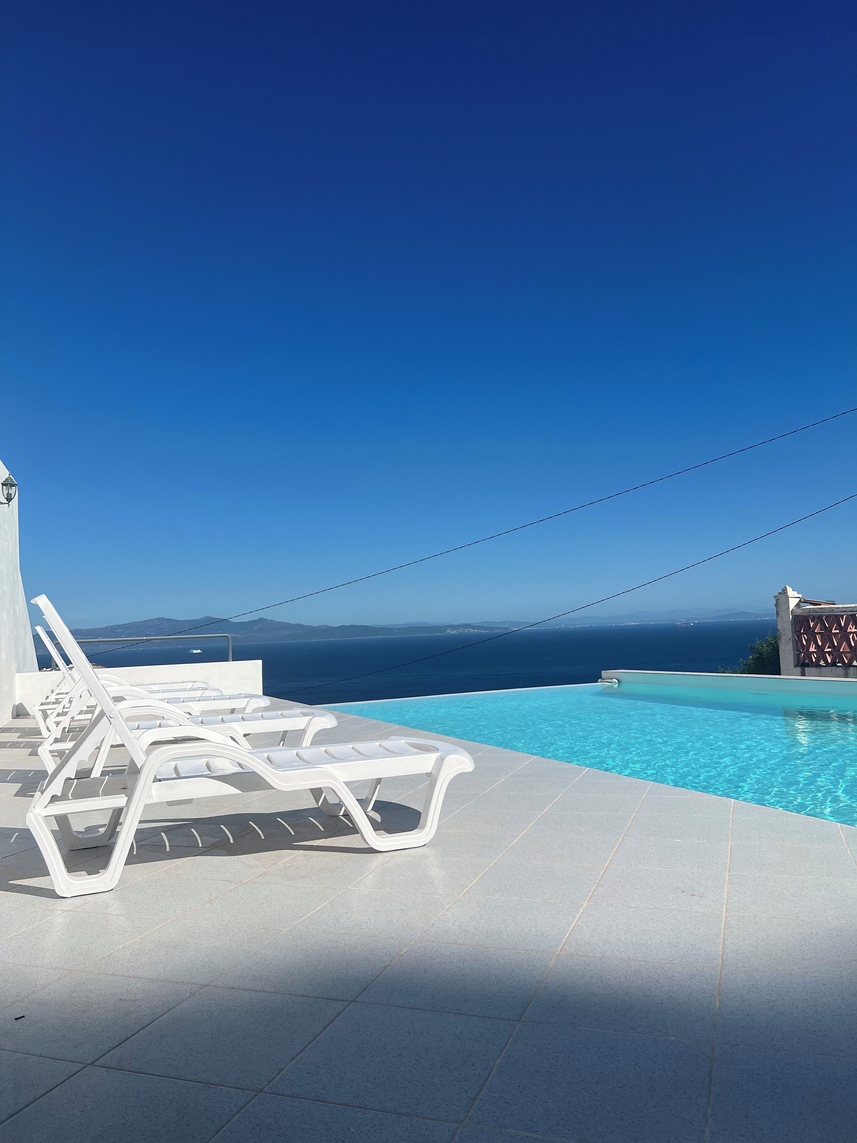 Area piscina con poltrone bianche, cielo azzurro e vista sul mare.