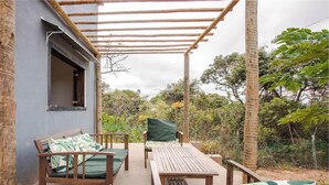 A covered outdoor seating area with a table and chairs, a wooden bench, and a window overlooking a garden. - Sítio em Jaboticatubas com Área de Lazer Completo (Jaboticatubas)