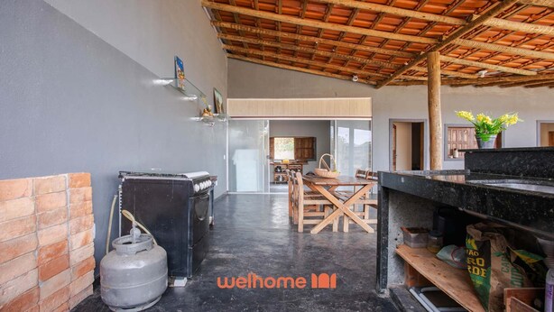 A well-lit kitchen with a gas stove, a refrigerator, and a gas cylinder. There is a dining area with a wooden table and chairs. - Sítio em Jaboticatubas com Área de Lazer Completo (Jaboticatubas)