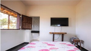 A small, simple room with a bed, a TV mounted on the wall, a wooden stool, and a fan. - Sítio em Jaboticatubas com Área de Lazer Completo (Jaboticatubas)
