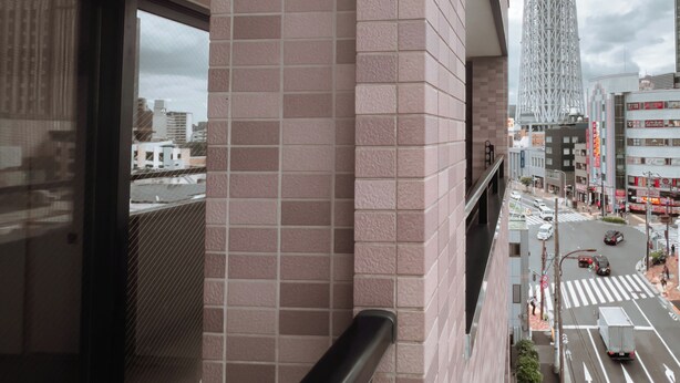 A high-rise building with a distinctive tower, a tiled wall, and a street view with vehicles. - Skytree Star 11 Hotel (Tokyo)