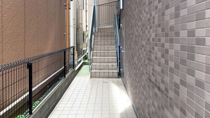 A narrow alleyway with a metal fence on one side and a tiled wall on the other. A staircase leads up to a door at the end of the alley. - Skytree Star 11 Hotel (Tokyo)