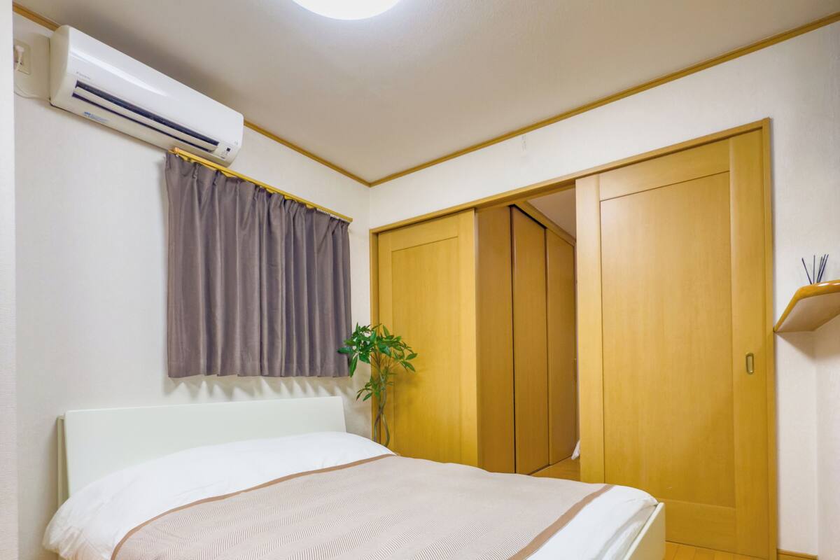 A bedroom with a bed, an air conditioner, a plant, and wooden wardrobes.