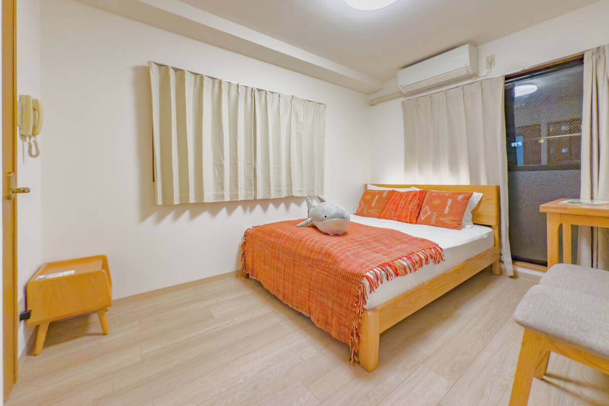 A bedroom with a bed, a small table, a chair, a telephone, and a window with curtains.