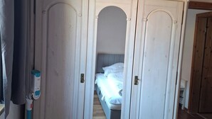 Une pièce avec une grande armoire blanche, un lit avec du linge de lit blanc et un plancher en bois.