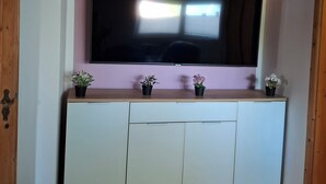 Une pièce dotée d’un grand téléviseur à écran plat fixé au mur, au-dessus d’un meuble de couleur claire muni de trois portes. Trois petites plantes en pot sont disposées sur le dessus du meuble.