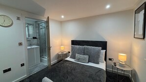 Ett modernt hotellrum med en stor säng, sänglampor, en väckarklocka och ett badrum med en glasdörr.
