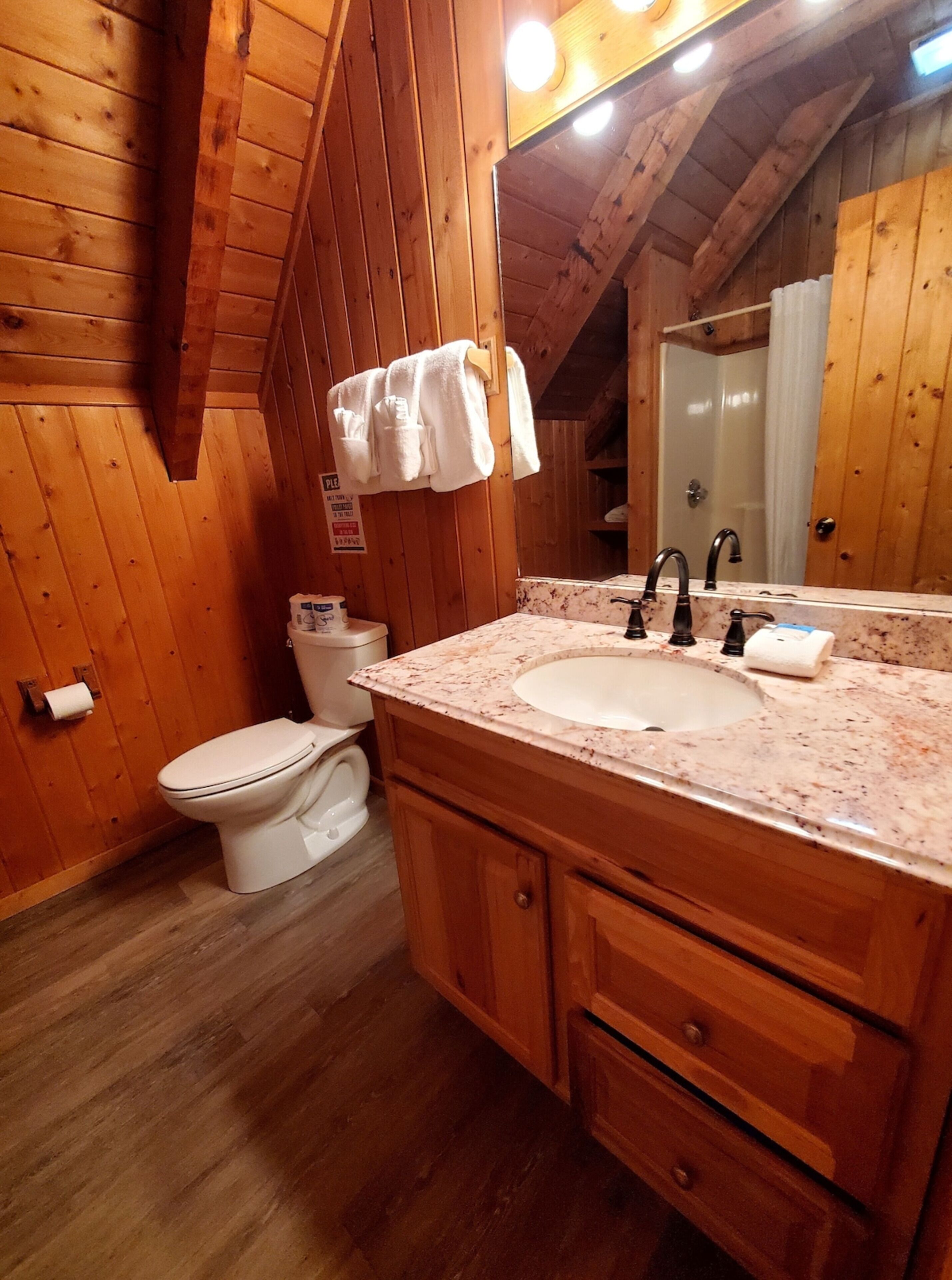Een houten badkamer in een blokhut, met toilet, wastafel en spiegel.