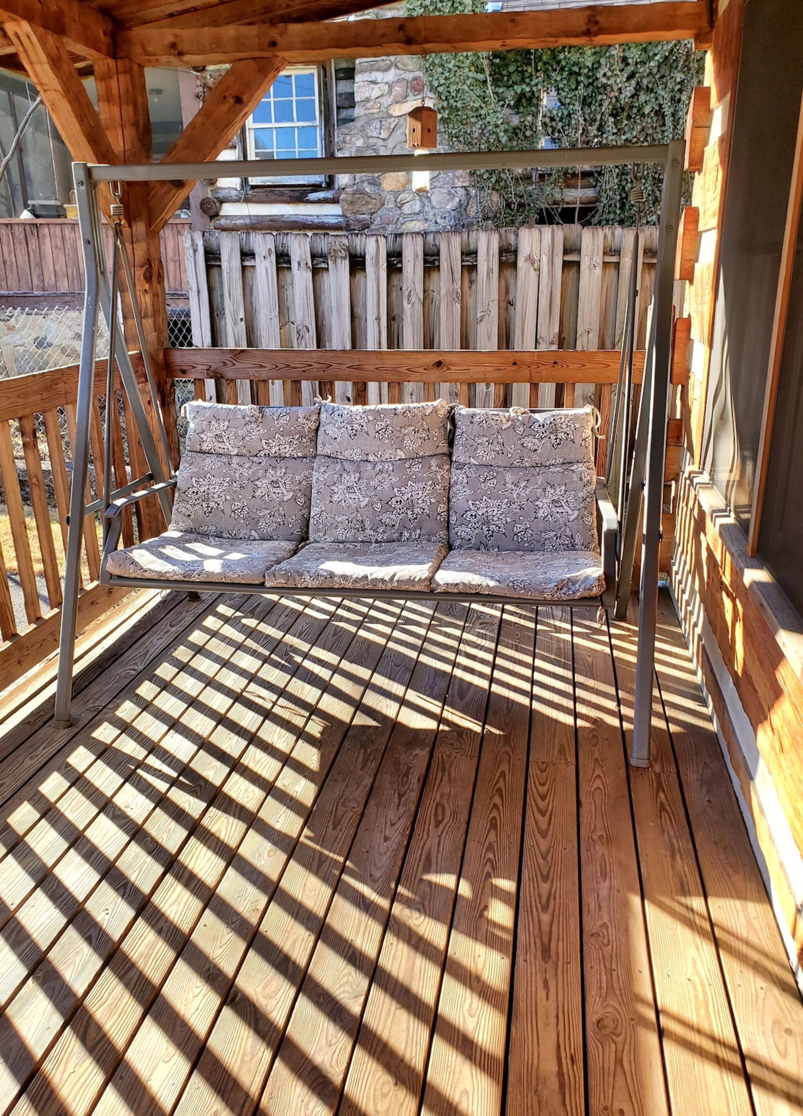 Een houten terras met een bank onder een houten pergola.