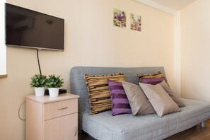 A modern living room with a grey sofa, two potted plants, and a flat-screen TV mounted on the wall.