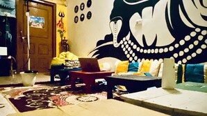 A living room with a large mural, a wooden coffee table, and a sofa with cushions. - Rudra Homestay (Varanasi)