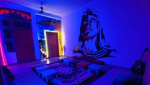 A room with a large mural, a bed, a sofa, a coffee table, and a guitar. - Rudra Homestay (Varanasi)