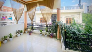 A spacious balcony with potted plants, a decorative ceiling, and a view of neighboring buildings. - Rudra Homestay (Varanasi)