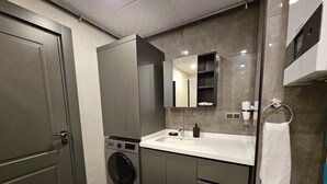 A modern bathroom with a built-in washing machine, a sink, and a mirror. - Professionally Maintained Spacious New Suites 2-1 (Antalya)