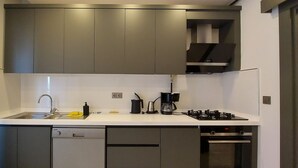 A modern kitchen with grey cabinets, a white countertop, a dishwasher, a coffee maker, and a stove.