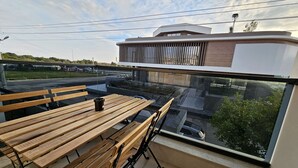 A balcony with wooden benches and a table, overlooking a parking area and a building with a modern design.