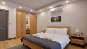 Un dormitorio con cama, mesitas de noche, armario, aire acondicionado y un cuadro en la pared.
