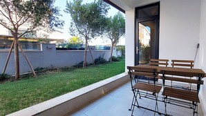 Un patio con una mesa y sillas, un pequeño césped y un edificio con puerta de vidrio.