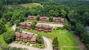 A cluster of brown multi-story buildings with balconies, surrounded by lush greenery and a hilly landscape. - 3 Bedroom Townhouse Across from Holimont (Ellicottville)