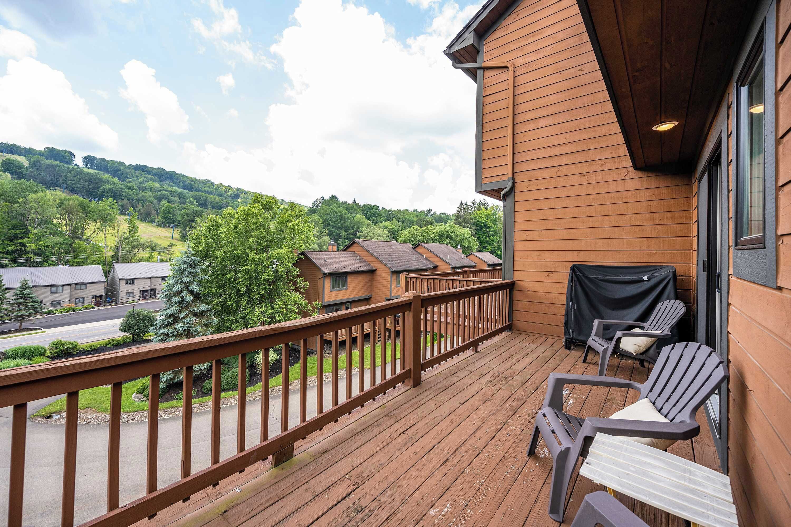 Una terraza de madera con mobiliario exterior y vistas a un paisaje montañoso.