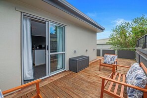 A wooden deck with outdoor seating, a sliding glass door, and a small outdoor kitchen area. - Tarawera Twins - Two Homes, Spa Pools, Sleeps 16 (Rotorua)