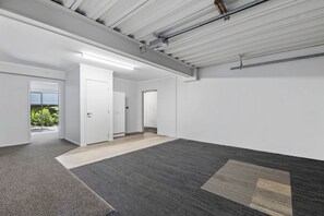 A spacious, modern room with a large window, a door leading to another room, and a ceiling with exposed ductwork.