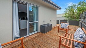 Una terraza de madera con mobiliario exterior, un ventanal corredero y una pequeña cocina al aire libre.
