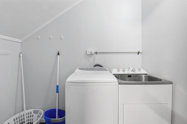 A laundry room with a washing machine, a sink, a mop, and a laundry basket.