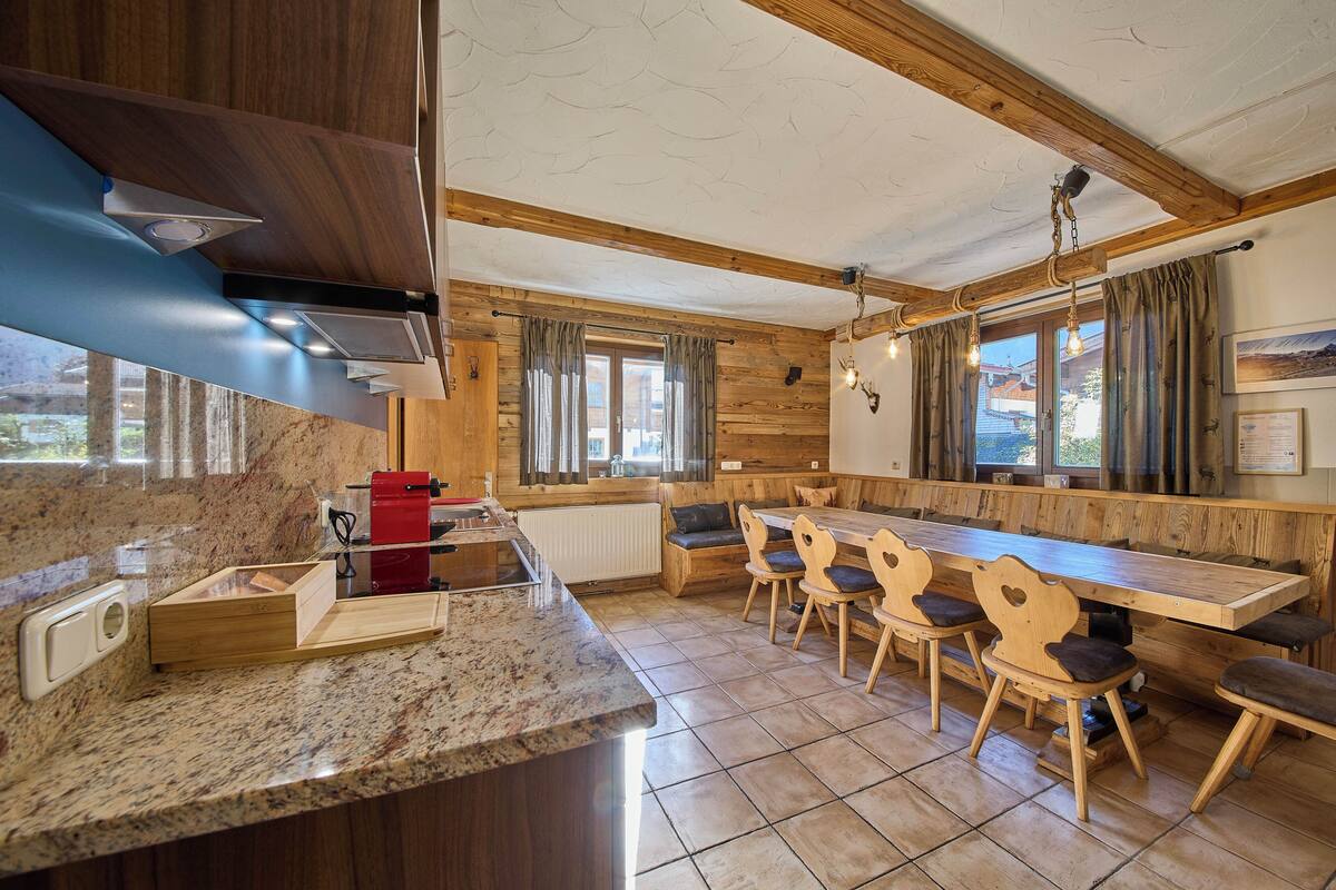 A kitchen with granite countertops, wooden cabinets, a built-in stove, and a dining area with wooden chairs and a long table.