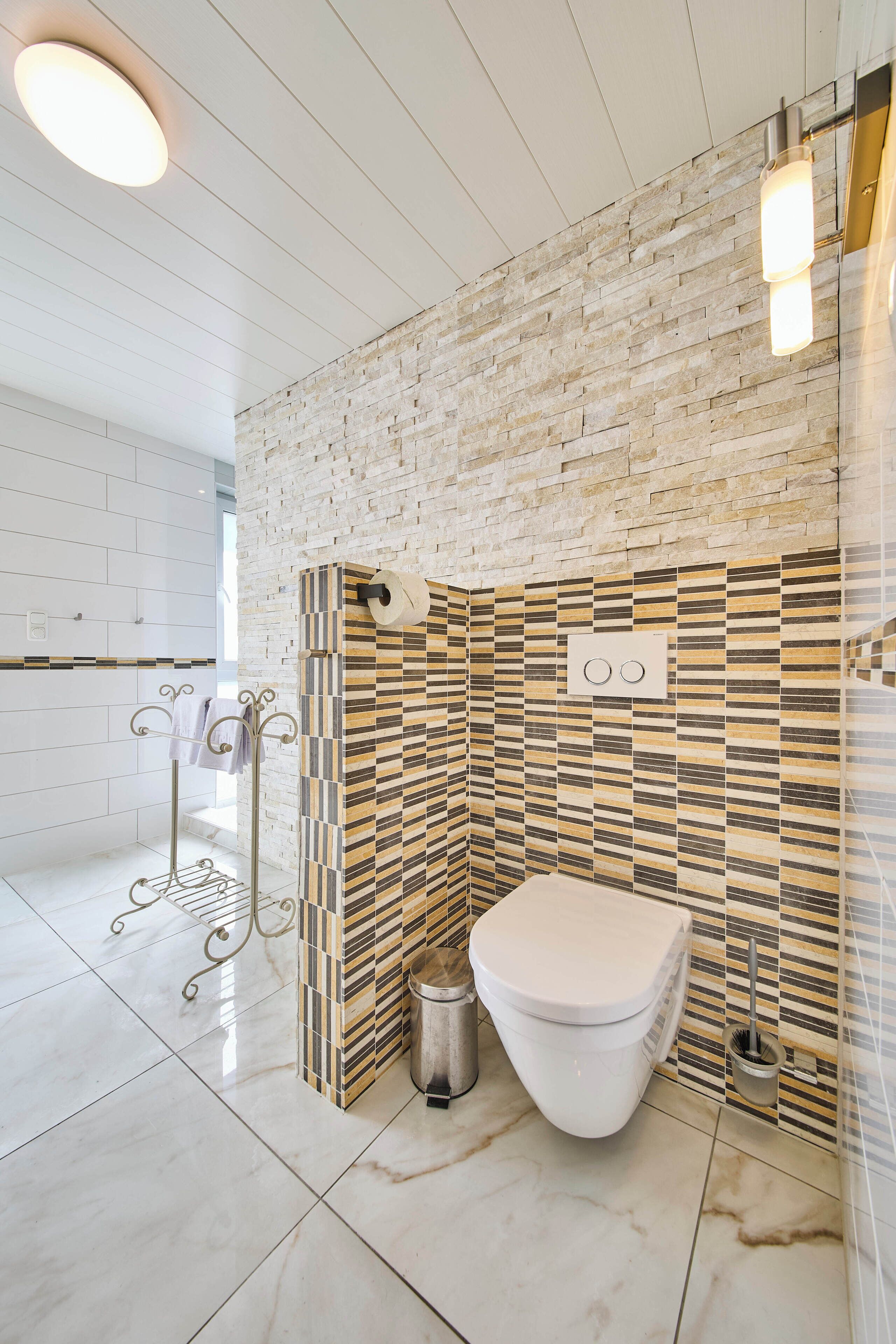 Une salle de bain moderne avec des toilettes blanches, un porte-serviettes en métal et un mur à motifs.