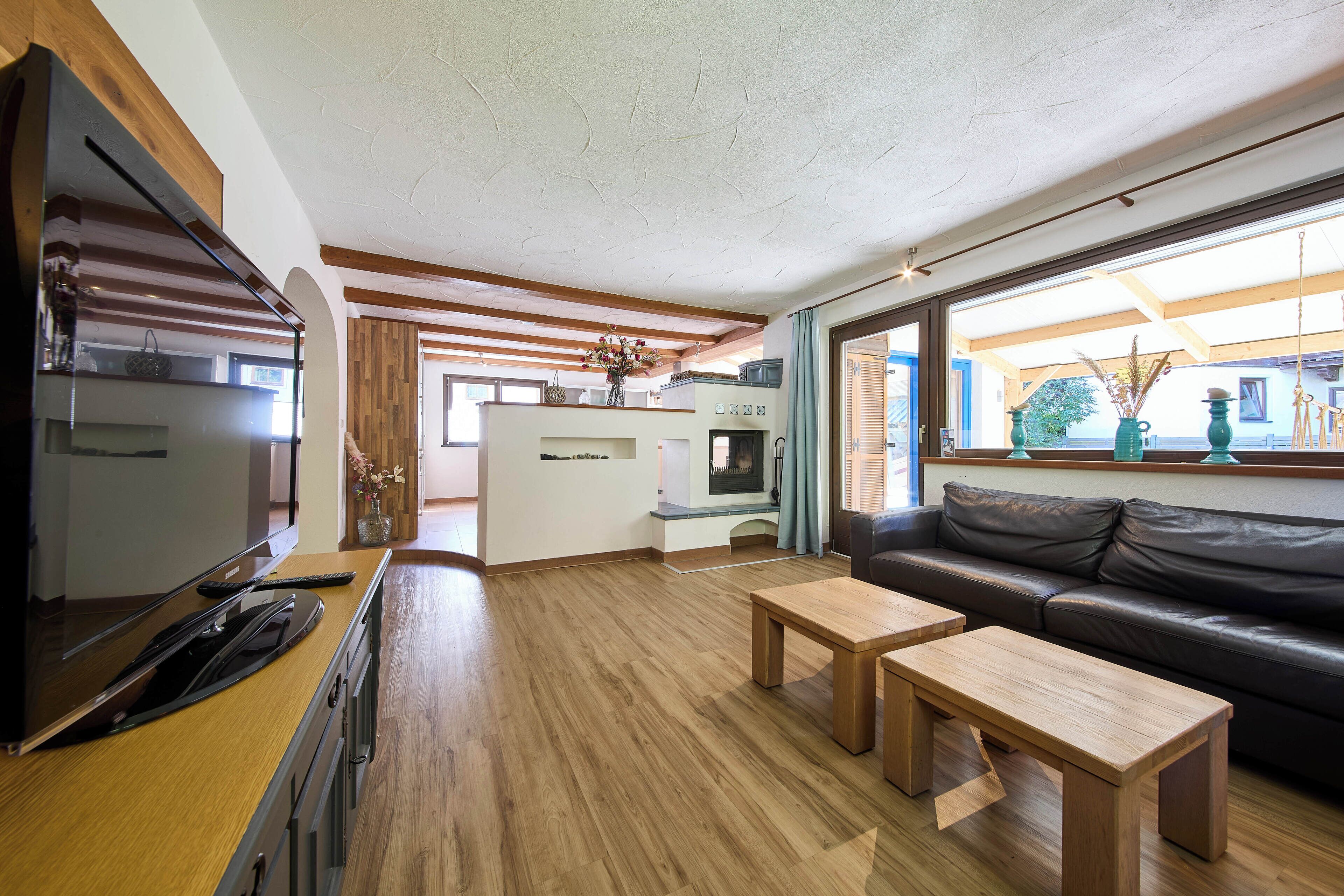 A modern living room with a wooden floor, a black leather sofa, two wooden coffee tables, and a TV on a wooden cabinet.