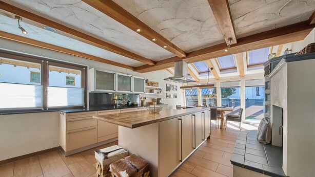A modern kitchen with a large island, wooden beams, and a skylight. - Apartments Enzian (Rauris)