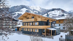 A multi-story wooden chalet with a balcony, set in a snowy mountainous area. - Apartments Enzian (Rauris)