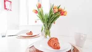 Una mesa con un croissant, un plato con un croissant, un jarrón con tulipanes y una taza blanca.