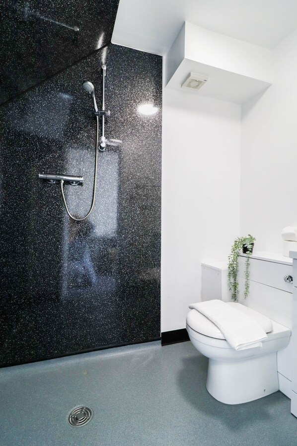Un baño moderno con pared de aspecto moteado en negro, un inodoro blanco y una cabina de ducha.