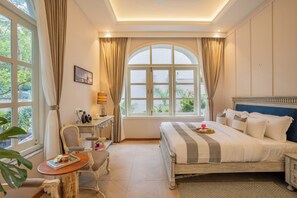 A bedroom with a large bed, a desk with a chair, a small table with a book, and a window with curtains. - Esh Cottages Birch | Hillside 4-BHK Hideaway With Lush Garden, Common Pool, & Gaming Zone (Calangute)