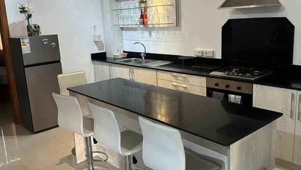 A modern kitchen with a central island, bar stools, stainless steel appliances, and pendant lighting.