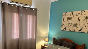 A bedroom with a bed, curtains, a wall clock, a nightstand, and a wall with a bird pattern.