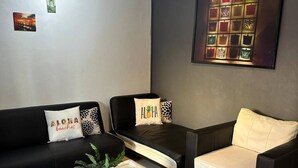 A modern living room with a black sofa, a white armchair, and a black coffee table. There are three wall-mounted artworks and a large framed picture above the sofa.