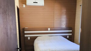 A room with a bed, wooden panel walls, a ceiling fan, and a window.