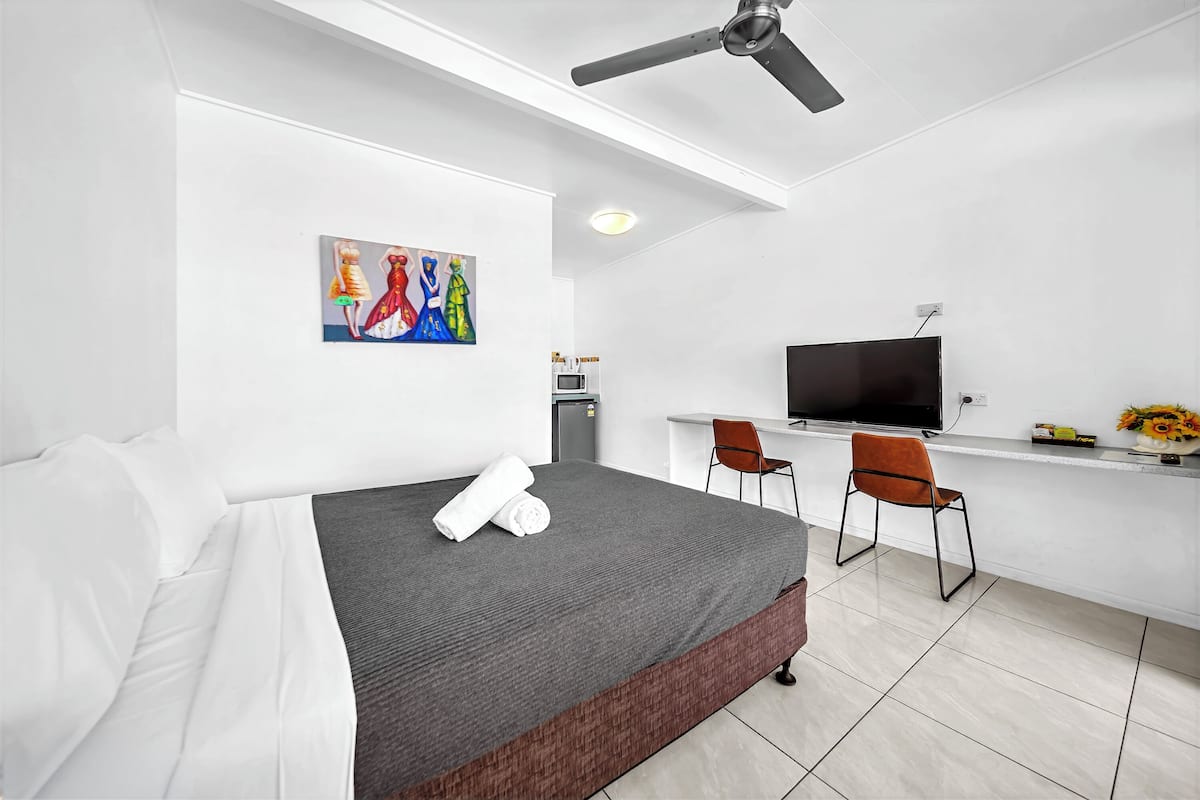 A modern hotel room with a bed, a desk, a television, and a painting on the wall.